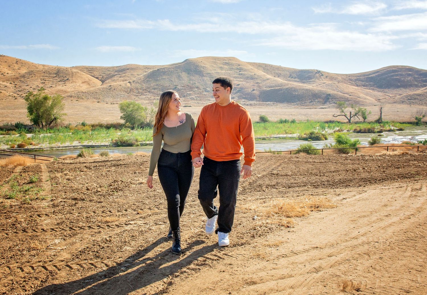 Couple walking hand in hand along a scenic desert mountain trail with golden sunlight.