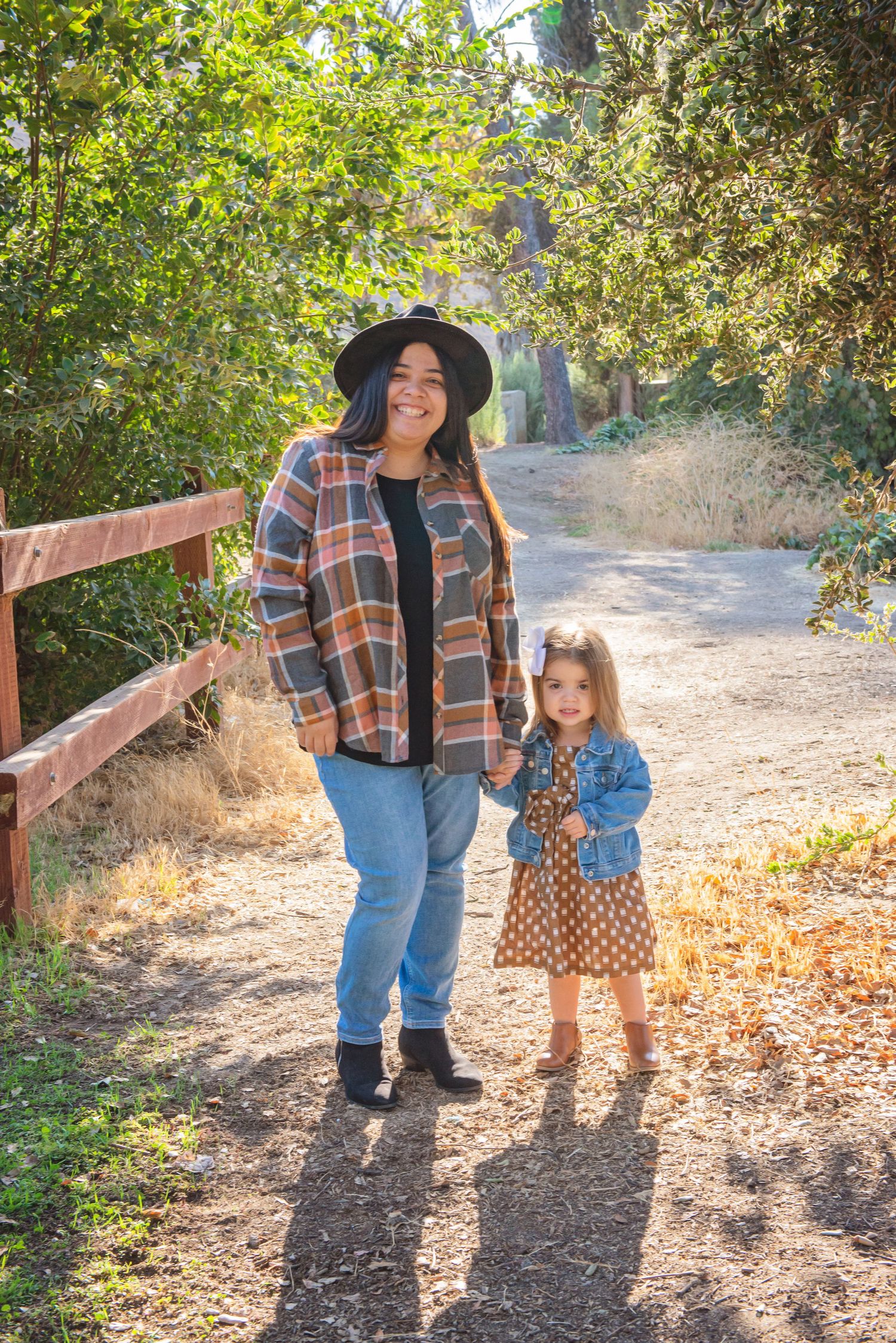 Parent and child walking along sunlit trail holding hands in autumn setting.