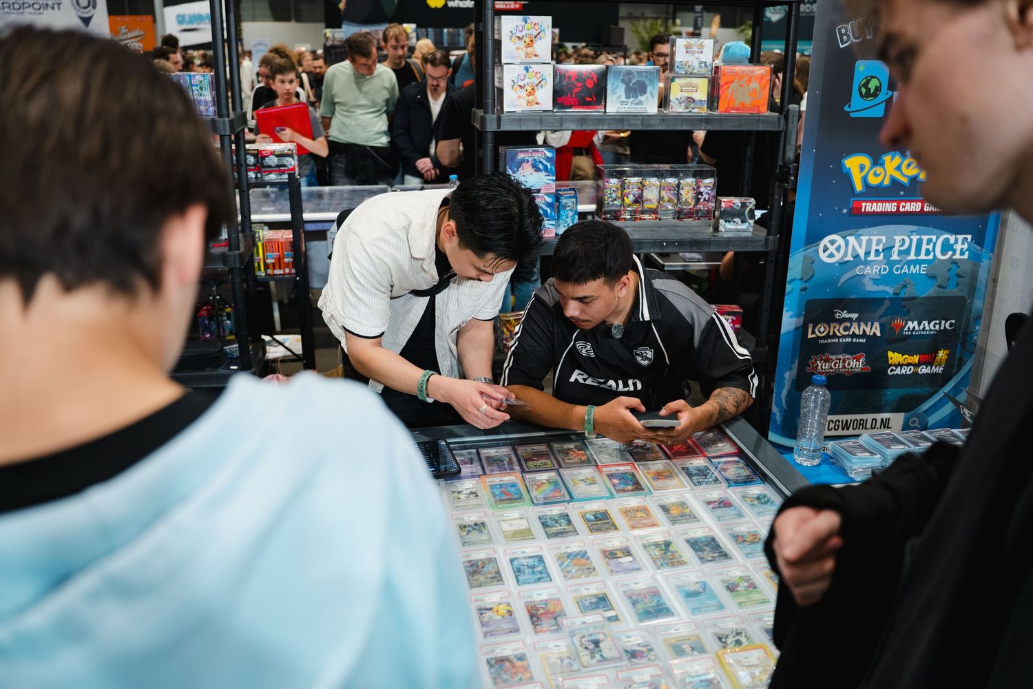 People browsing trading cards at a game store with Pokemon and One Piece merchandise visible on shelves.
