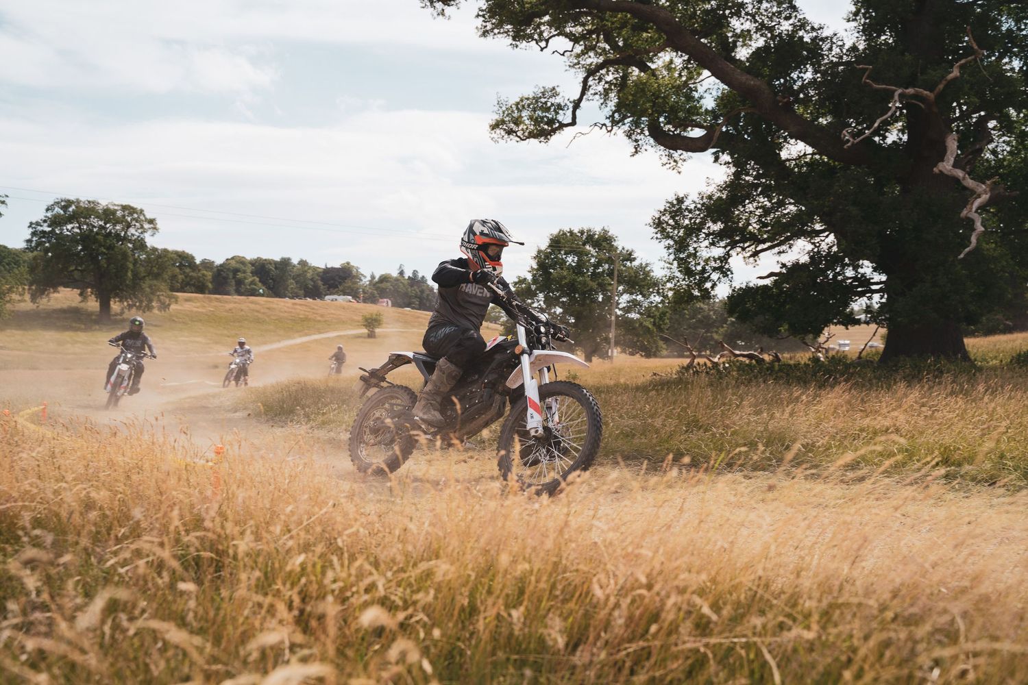 Dirt bike rider traversing through golden grass field with trees in background.