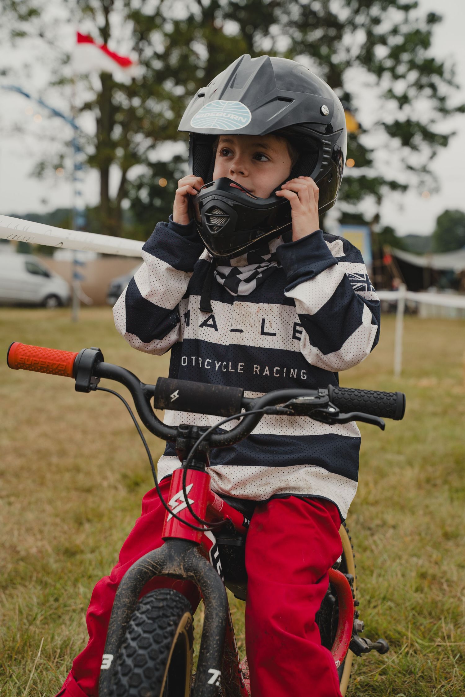 Young rider adjusting protective helmet while seated on a red bicycle.
