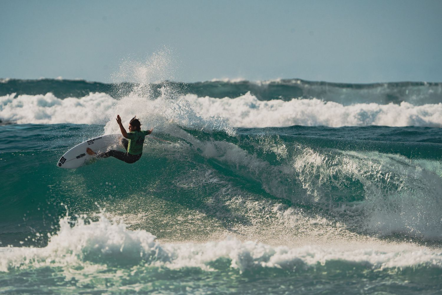A surfer rides through a breaking wave in turquoise ocean water.