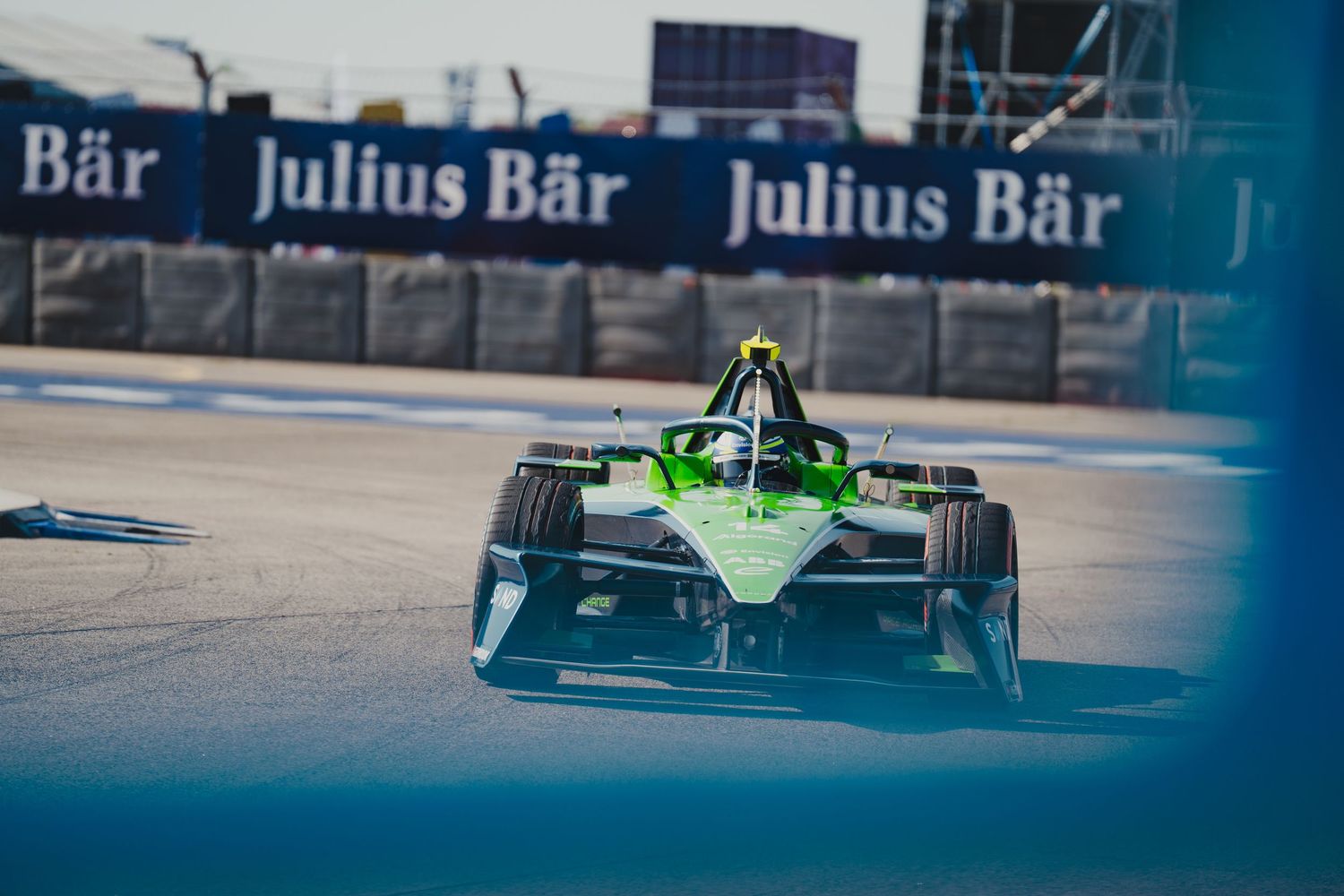 Green Formula E race car speeding on track with Julius Bär sponsorship banners in background during electric street racing event.