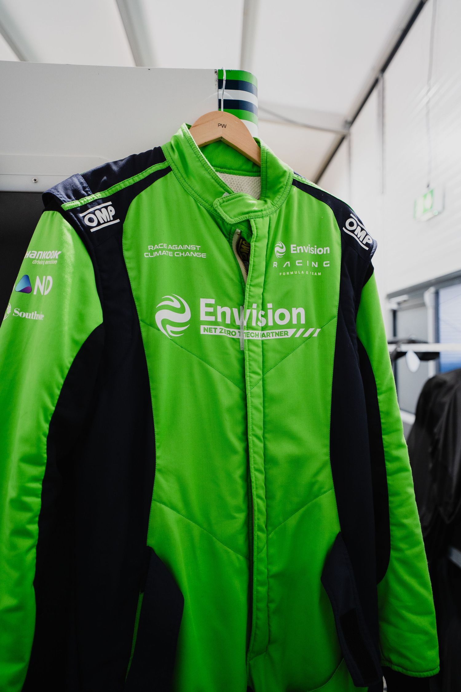 Bright green Envision Racing motorsport jacket on a hanger, featuring black accents and OMP branding.
