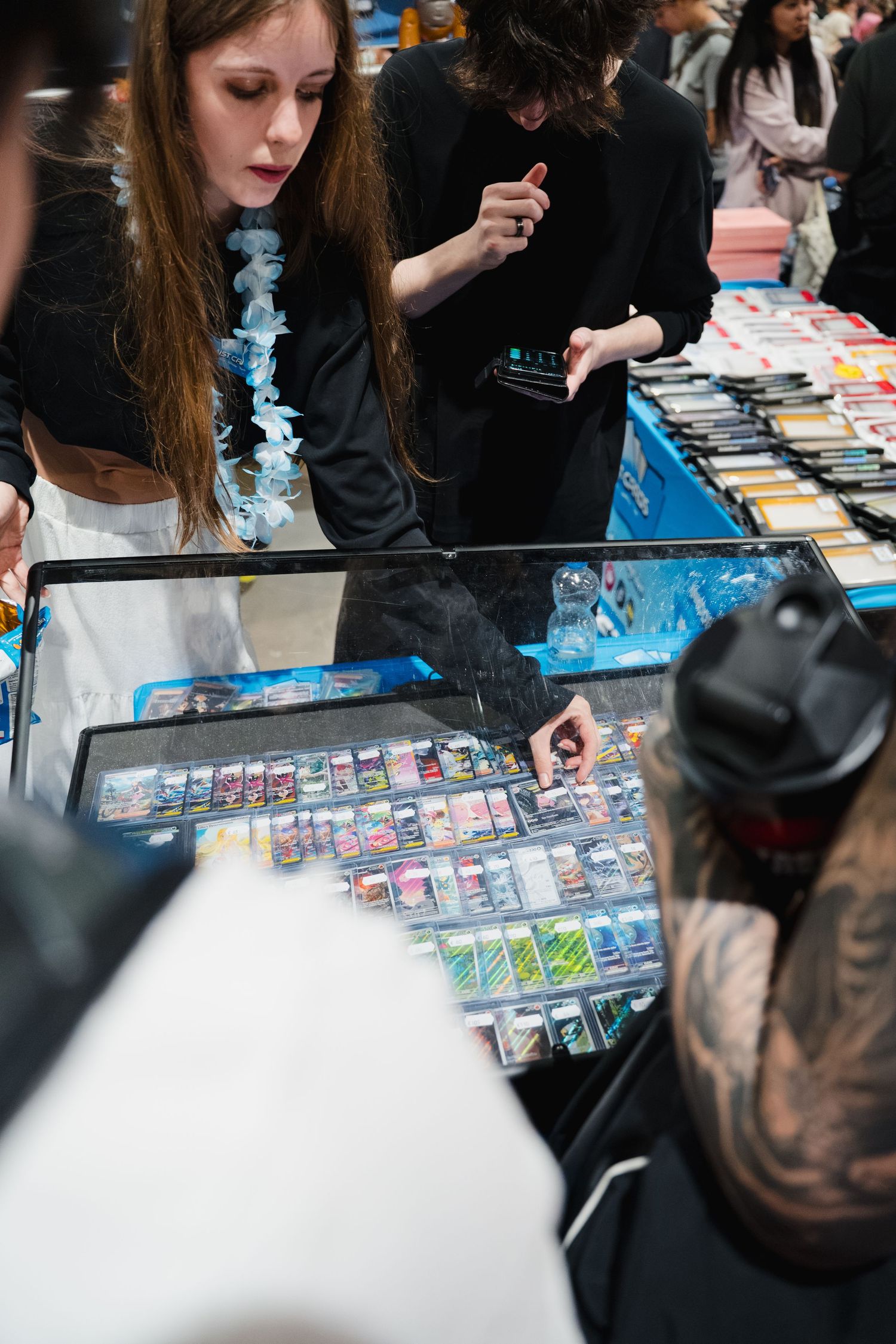 Woman browsing trading cards in a glass display case at a busy convention vendor booth.