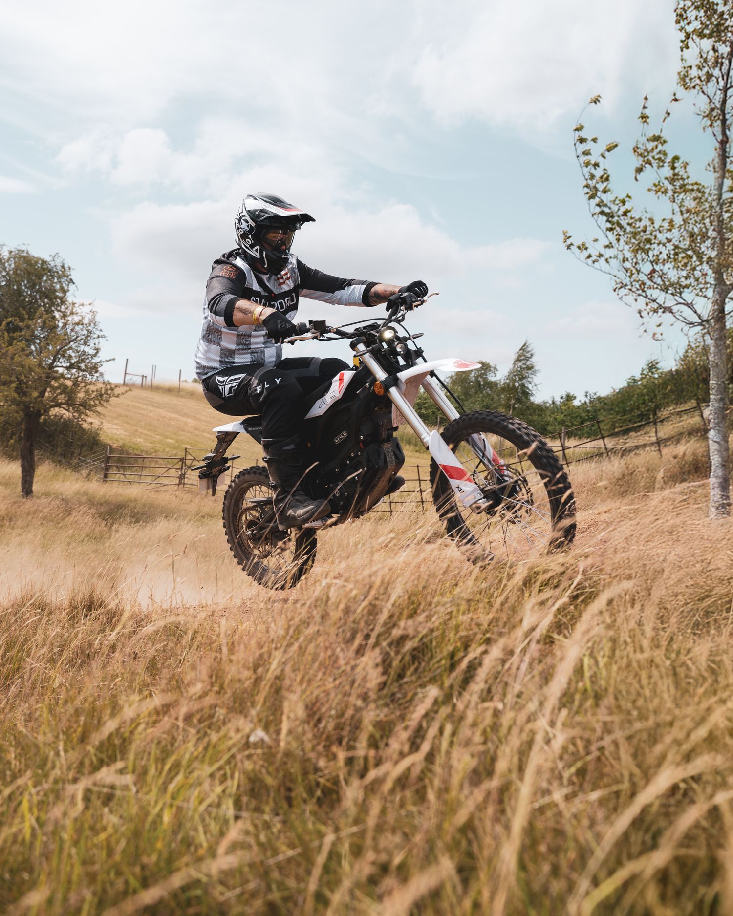 Motocross rider performing jump on dirt bike over dry grass terrain.