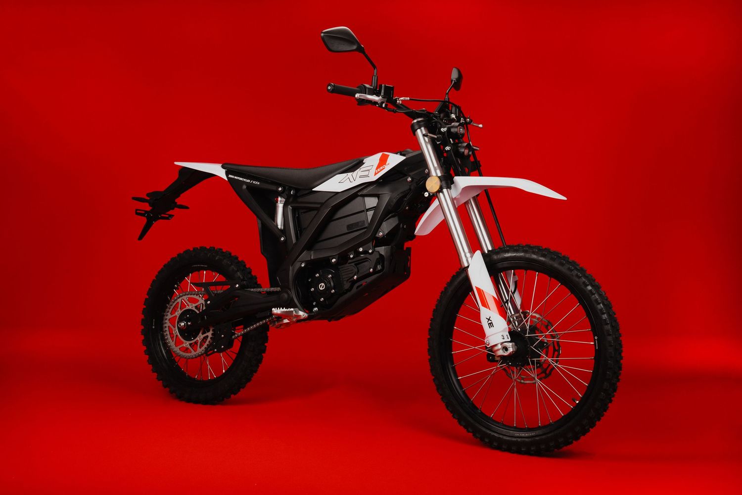 Black and white electric dirt bike photographed against vibrant red backdrop.