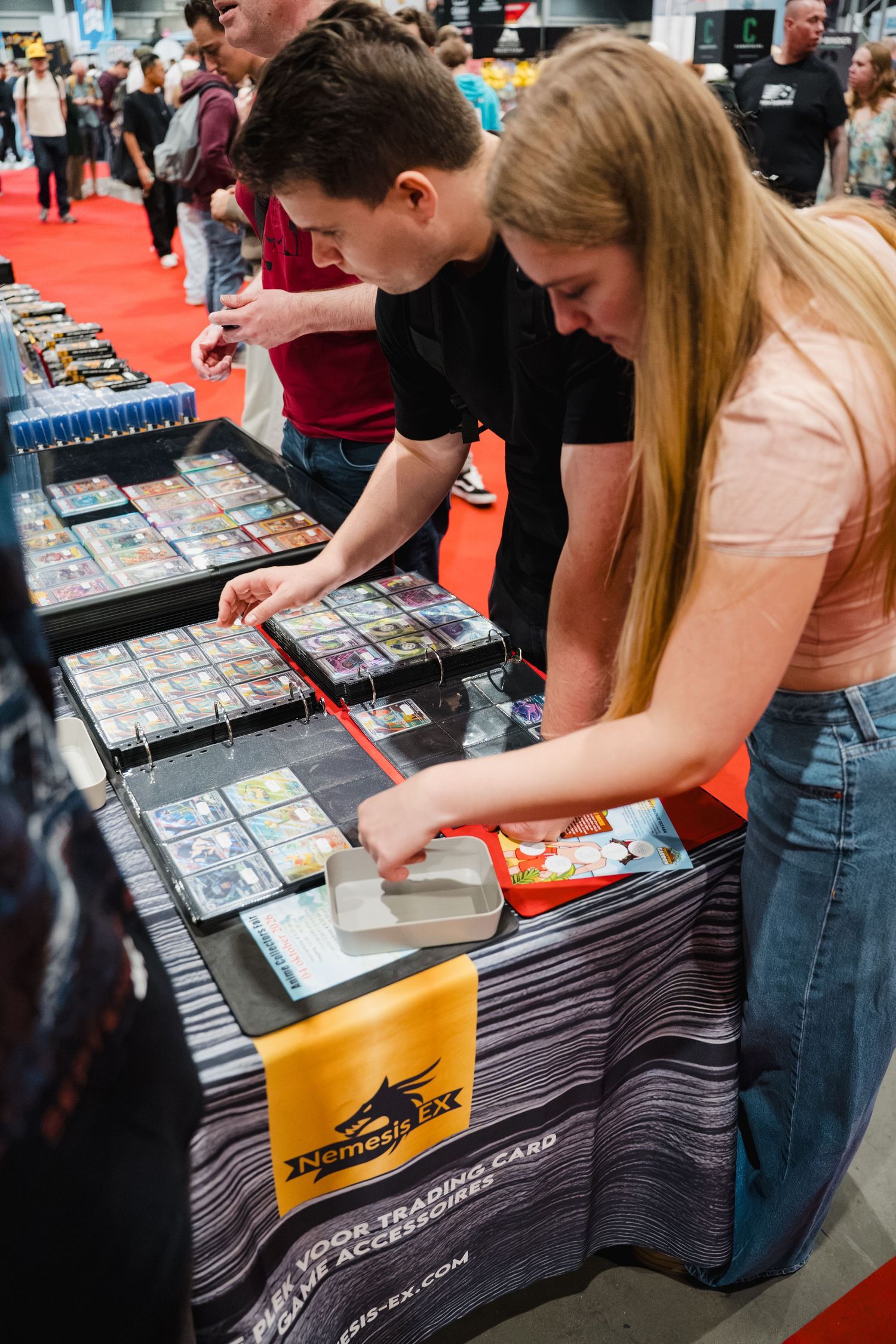 Two people browsing trading cards at a NemesEX booth during a card collecting convention.