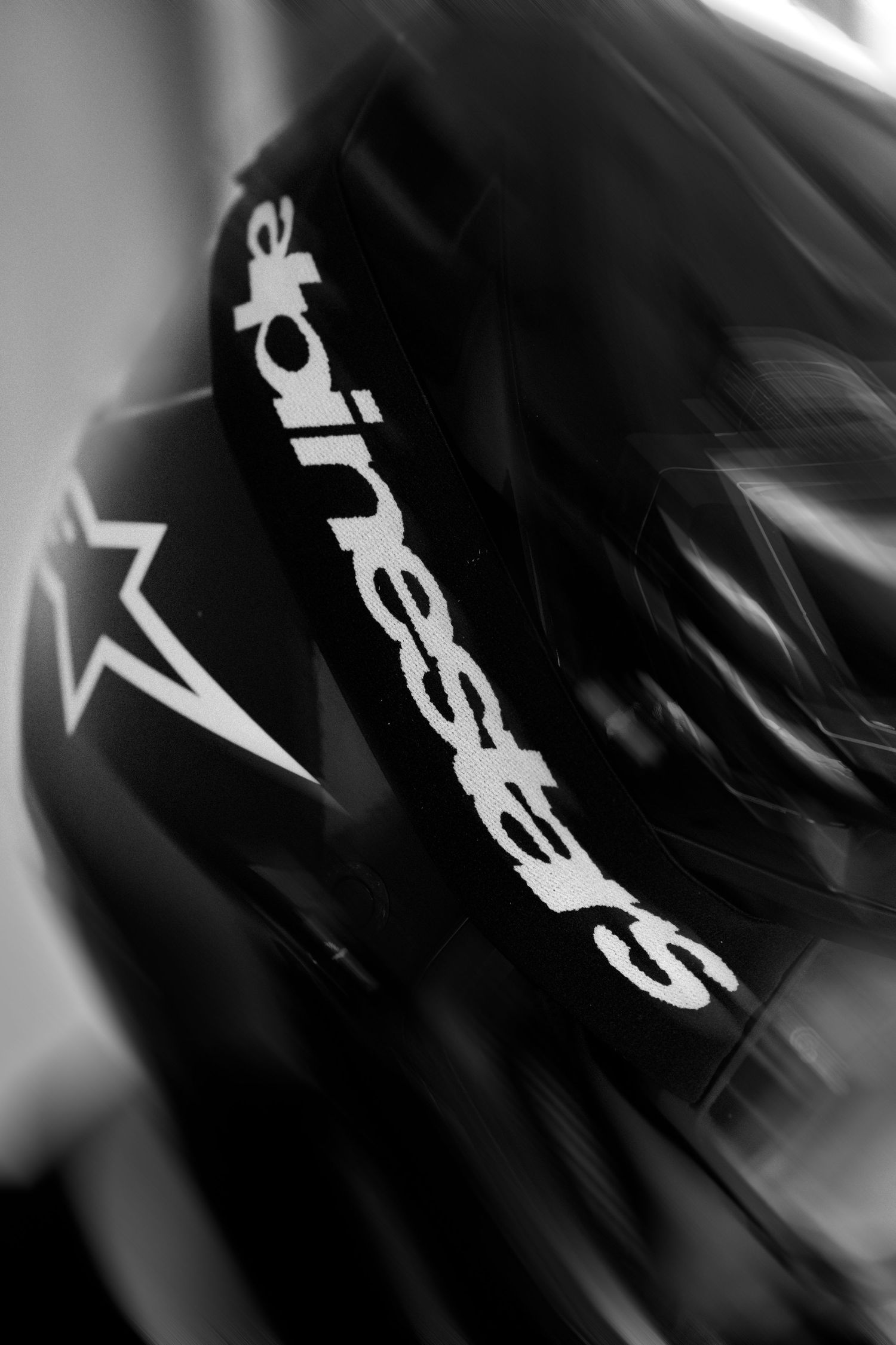 Black Alpinestars motorcycle helmet close-up in black and white photography showing brand logo detail.
