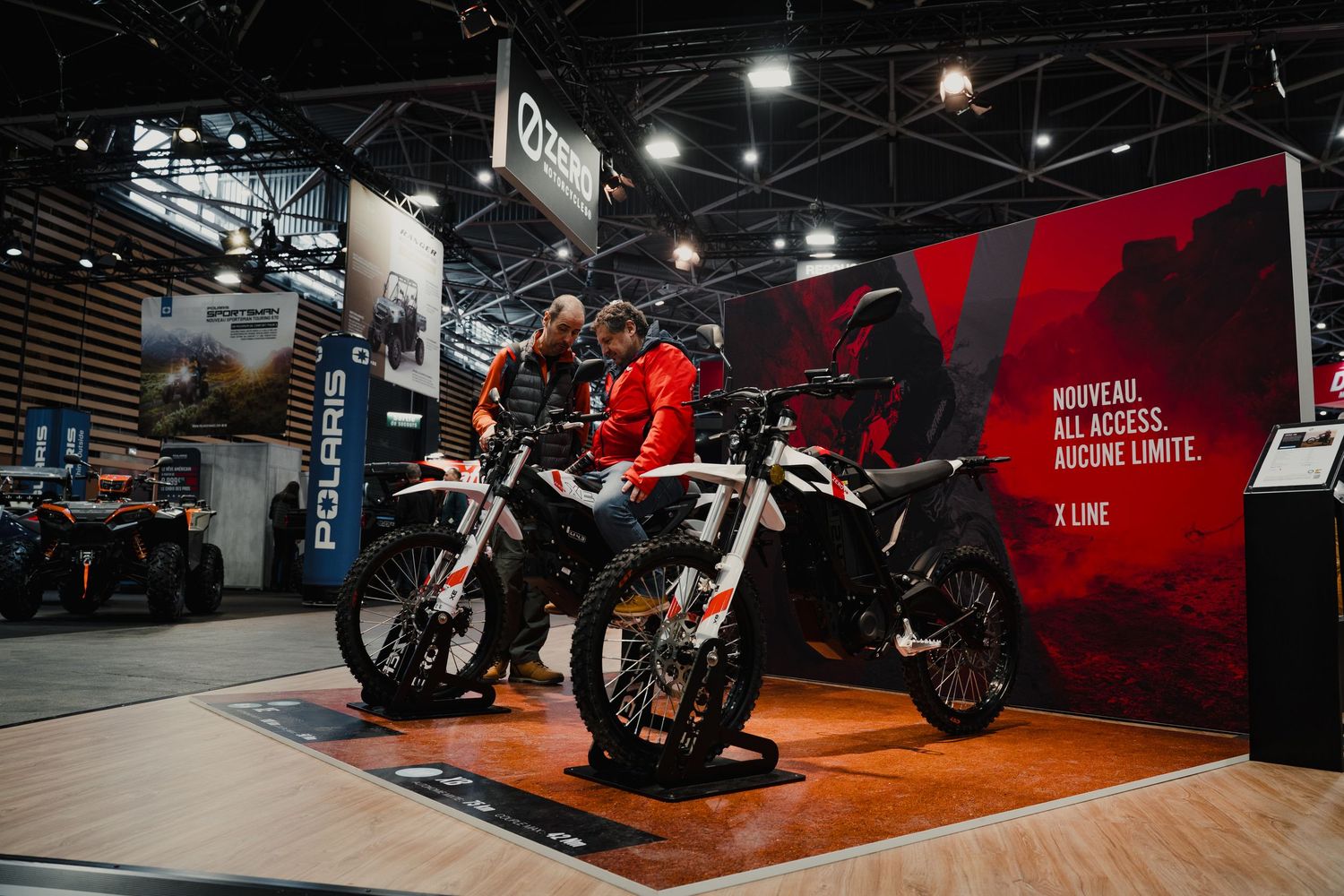 Modern motorcycles displayed on orange platform stages at an indoor motorcycle show.