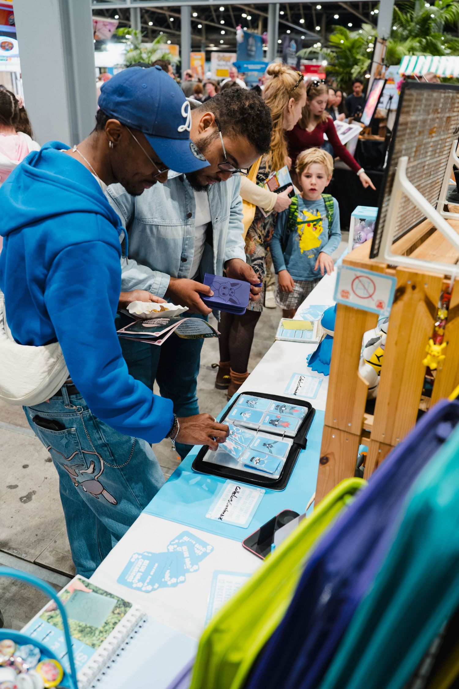 People browsing an interactive tablet display at a busy indoor expo or convention booth with blue themed materials.