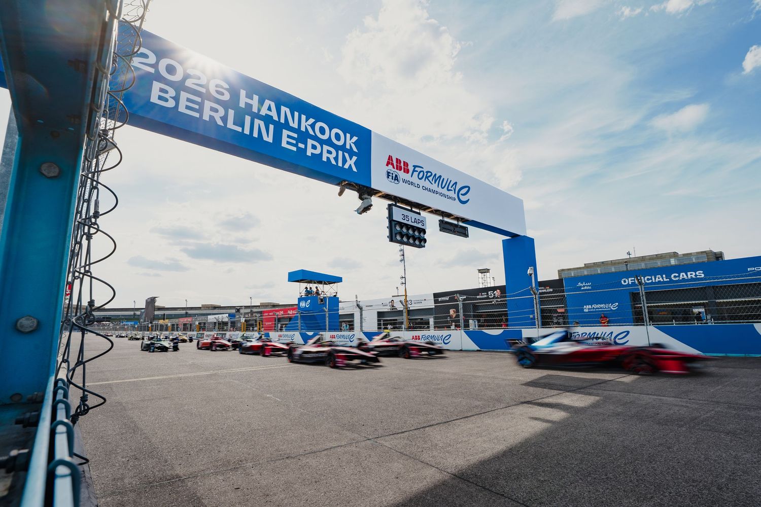 Formula E cars racing at the 2023 Hankook Berlin E-Prix under the start finish banner at Tempelhof Airport.
