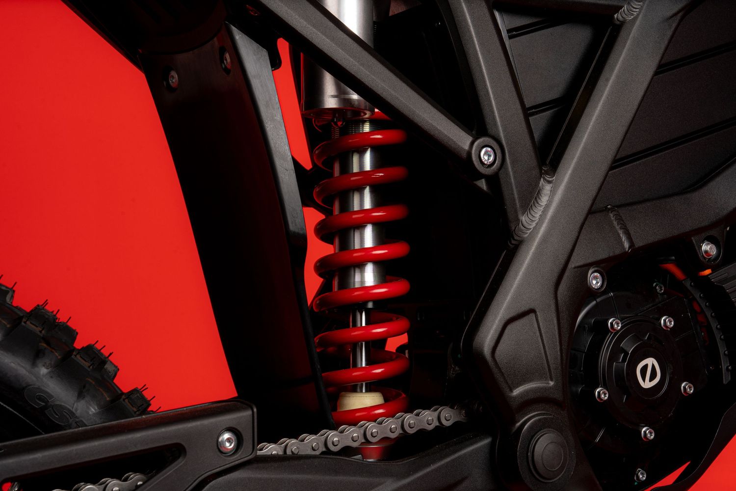 Close-up detail of a red and black motorcycle suspension system against a dramatic red background.