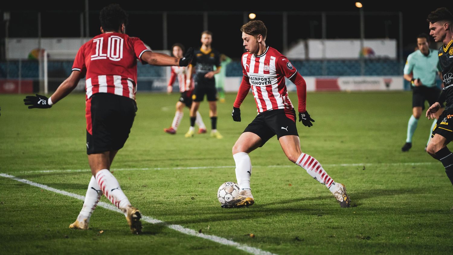 Players in red and white striped jerseys battle for possession during a nighttime soccer match.
