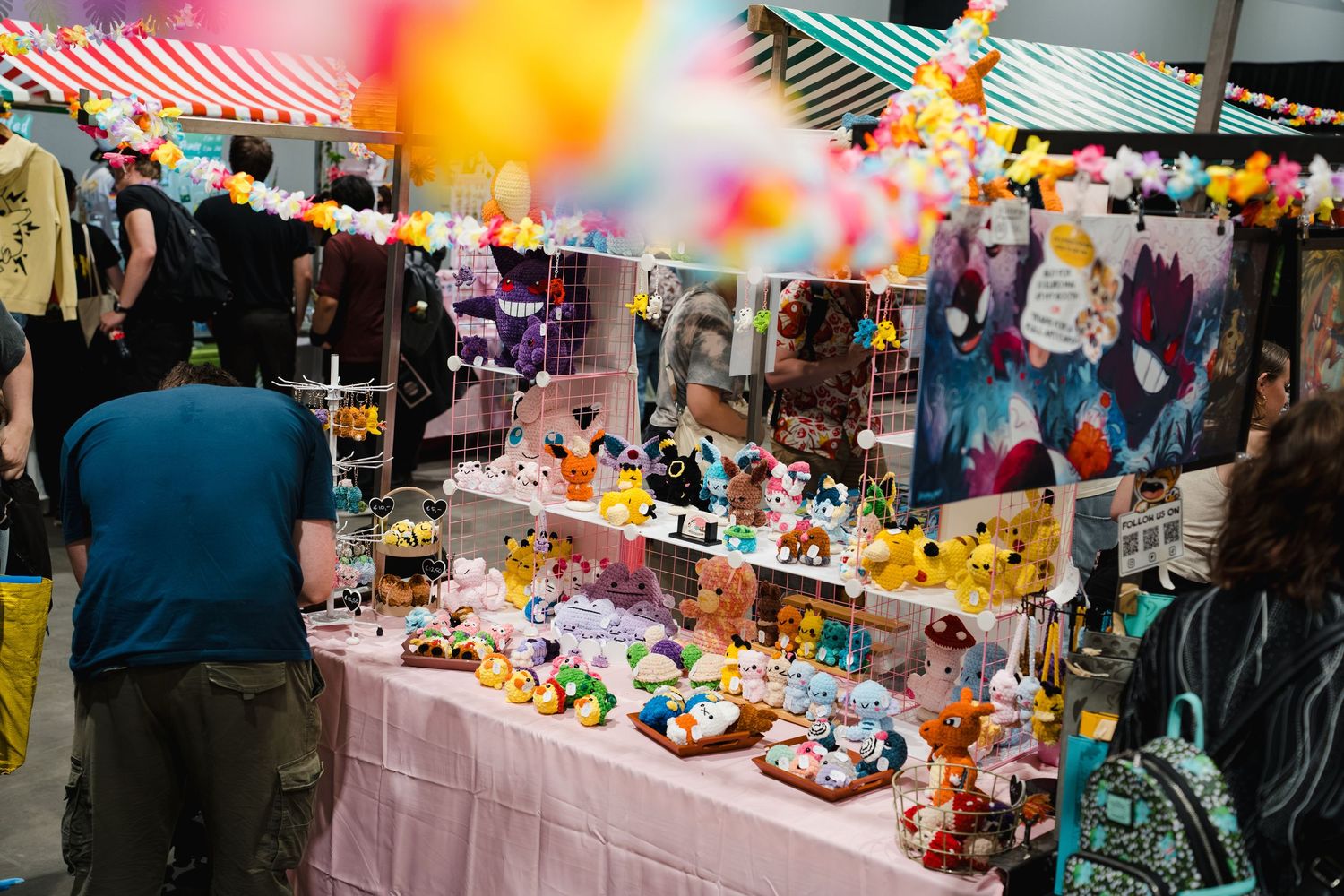 Colorful anime merchandise booth at a convention with Pokemon figures, plush toys, and decorative items on display.