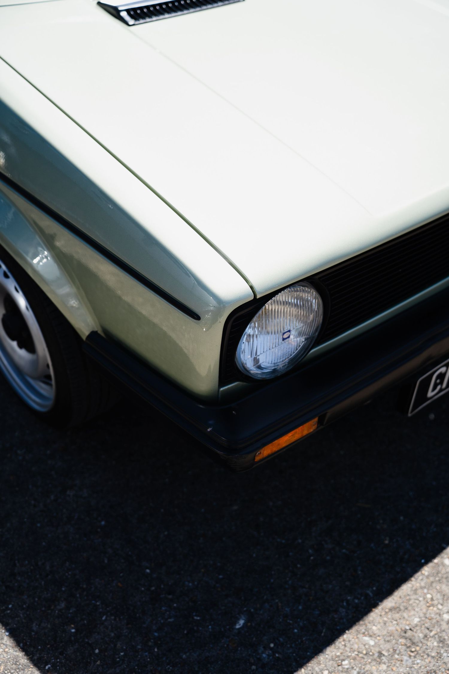 Close-up of a classic light green Volkswagen Golf MK1 front corner, showcasing its round headlight and clean bodywork.