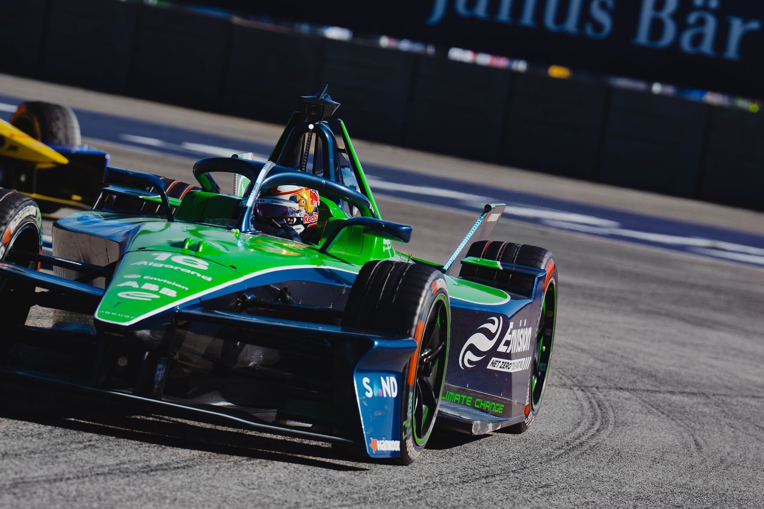 A green Formula E electric racing car speeds around a street circuit corner during a competitive race event.