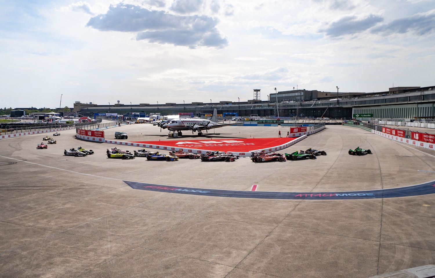 Formula E race cars lined up on a circuit at an airport venue with terminal building in the background.