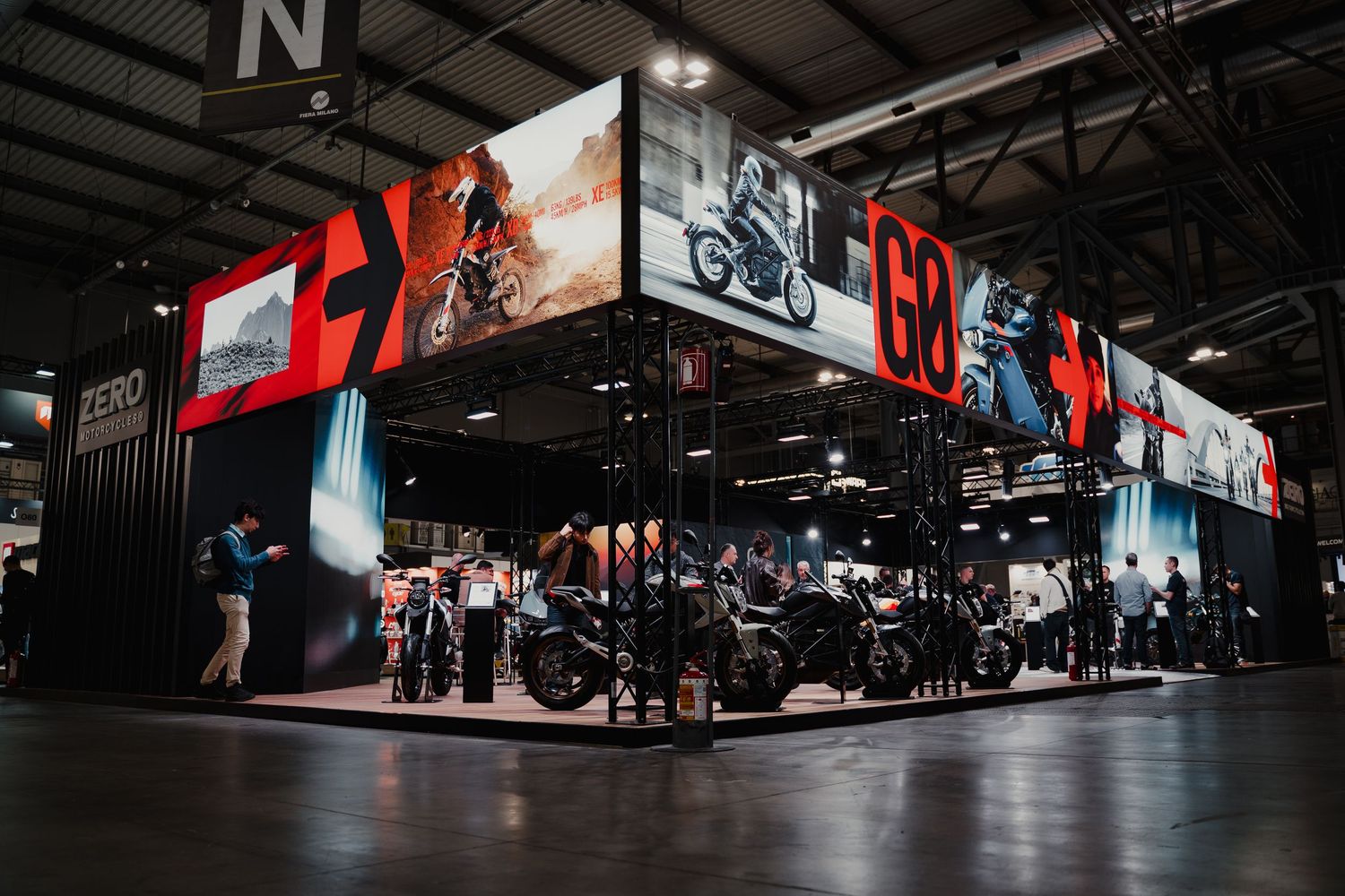 Wide panoramic view of a dimly lit motorcycle exhibition hall with displays and signage.