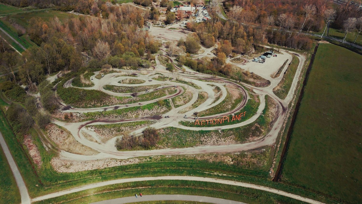 Aerial view of a winding motocross dirt track surrounded by trees and green fields.