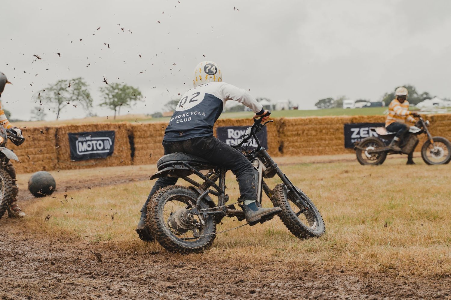 Vintage motorcycle parked on dirt track with other bikes in background.