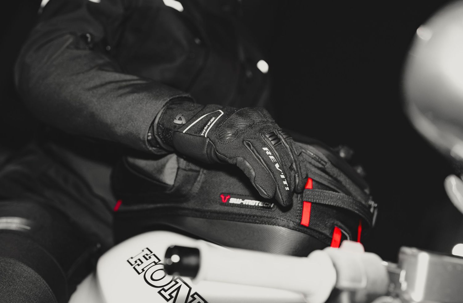 Black motorcycle gloves with red accents worn by a rider gripping handlebars, showcasing protective riding gear.