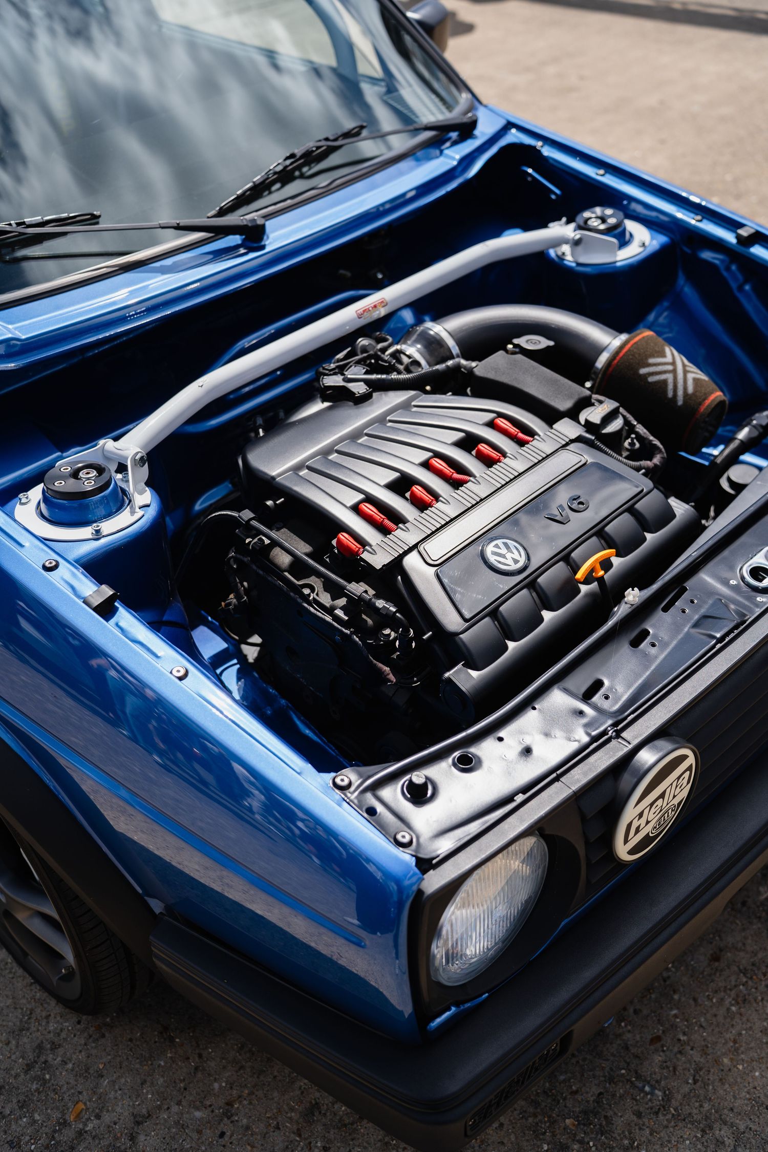 Blue Volkswagen Golf with hood open revealing a VW V6 engine swap with red accents and performance modifications.