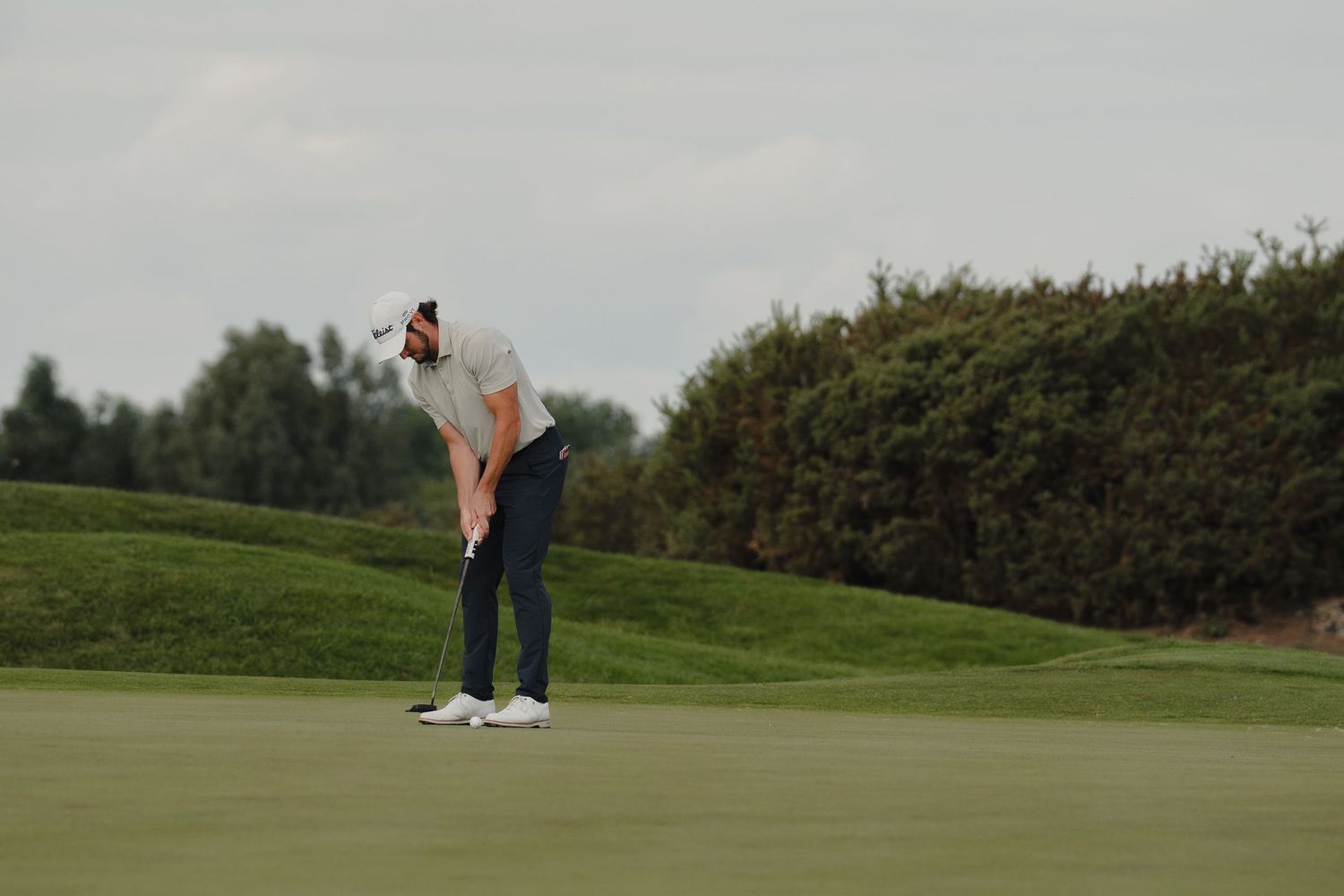 Golf course scene showing players on the green surrounded by manicured grass.