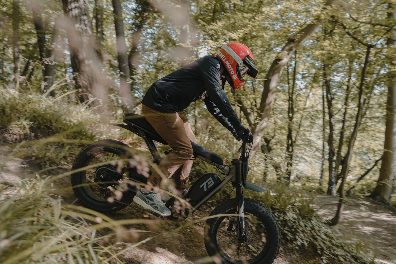 A motorcyclist performs a dynamic jump on a dirt bike through a wooded forest trail.