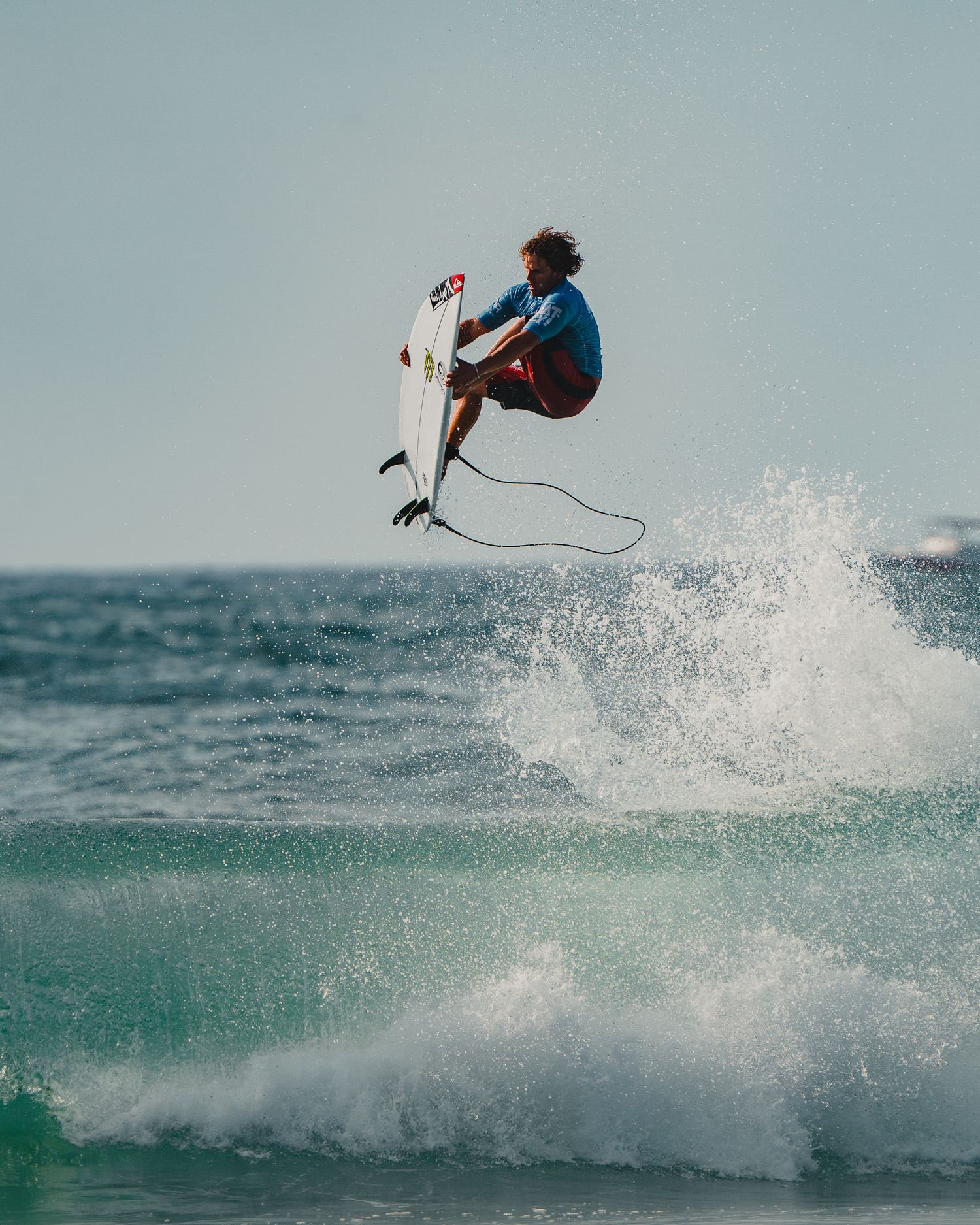 A surfer performs a high-flying aerial trick above the breaking wave.