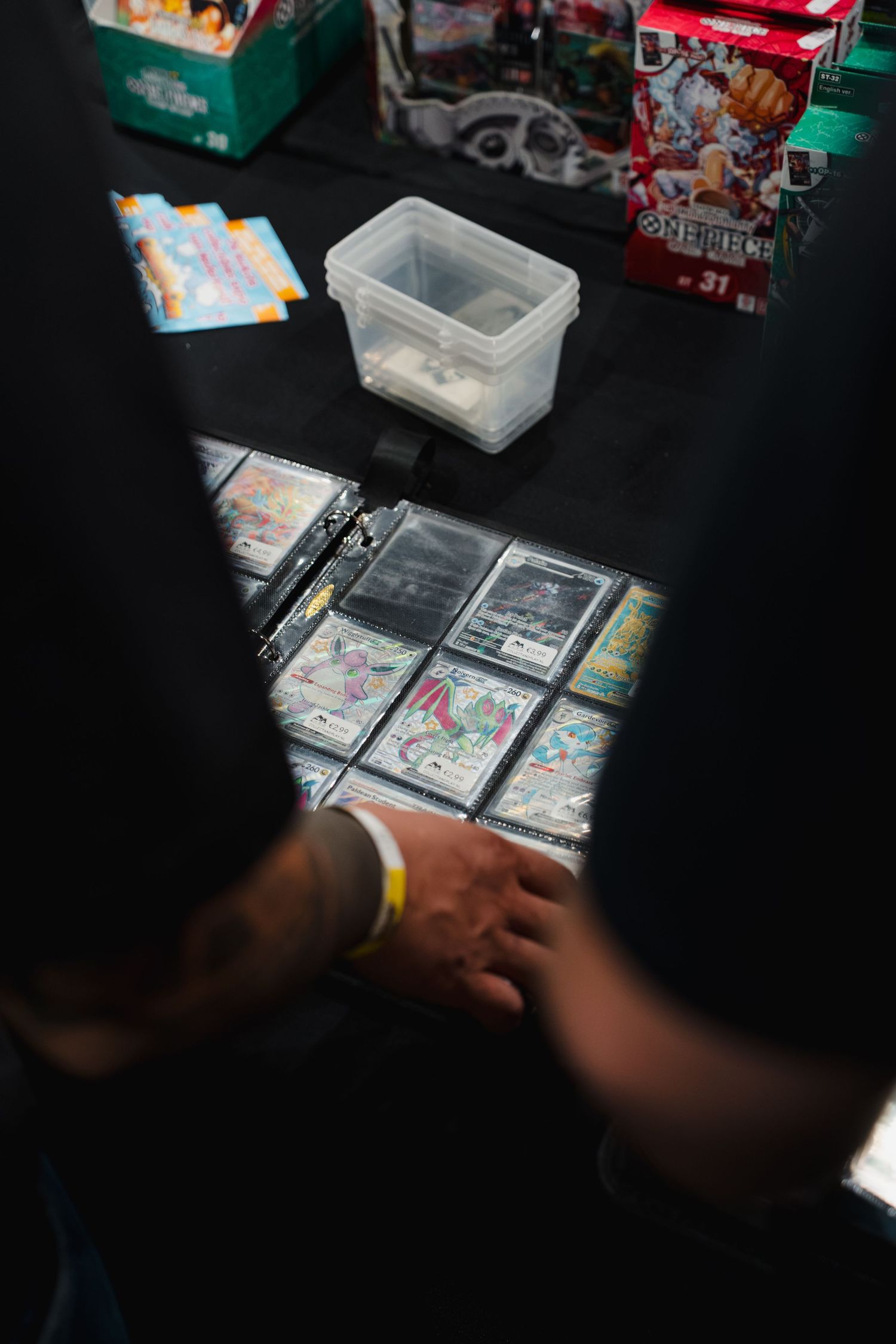Person browsing trading cards in protective sleeves at a card game convention vendor table.