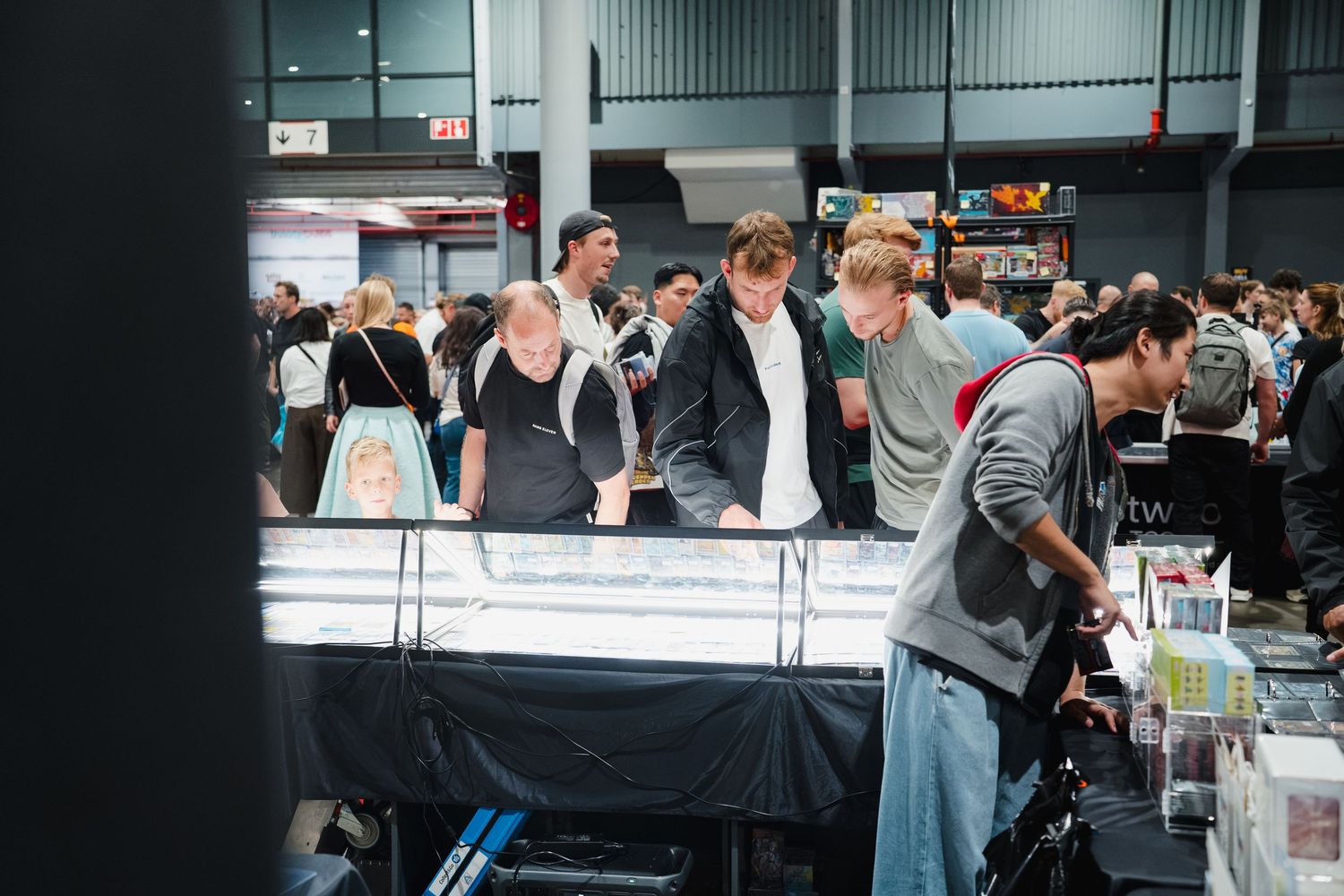 Shoppers browsing display cases at a busy indoor market or convention vendor hall.