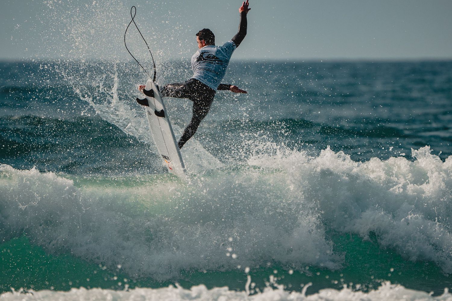 A surfer launches into an aerial maneuver above the ocean spray.