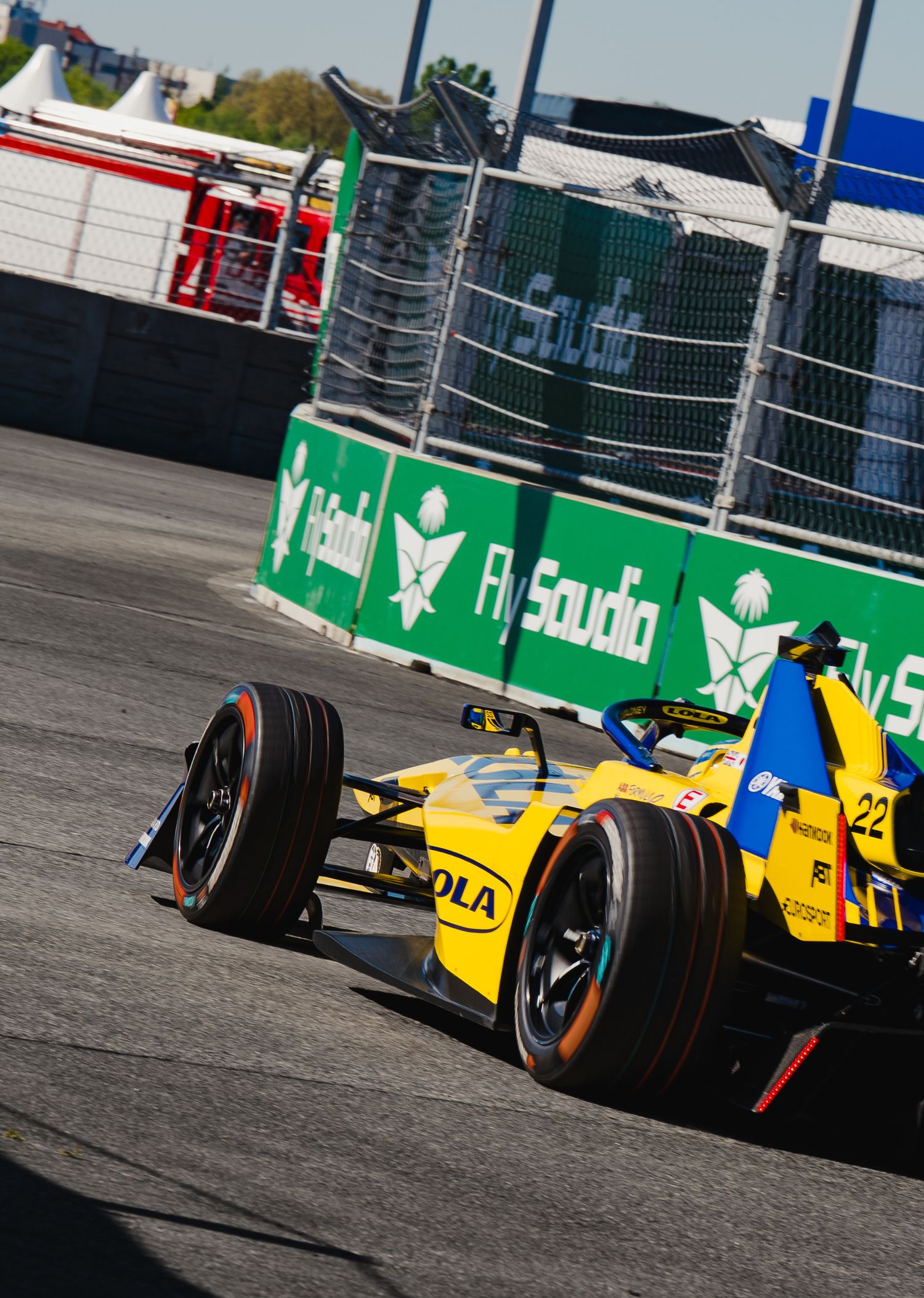 Yellow Formula E car number 22 races on a street circuit past Fly Saudia advertising boards.