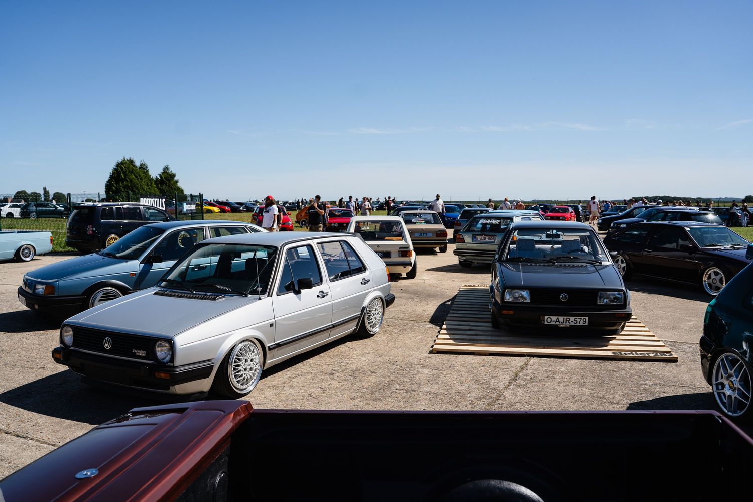 Vintage VW Golf and classic cars parked at an outdoor car show on a sunny day with spectators in the background.