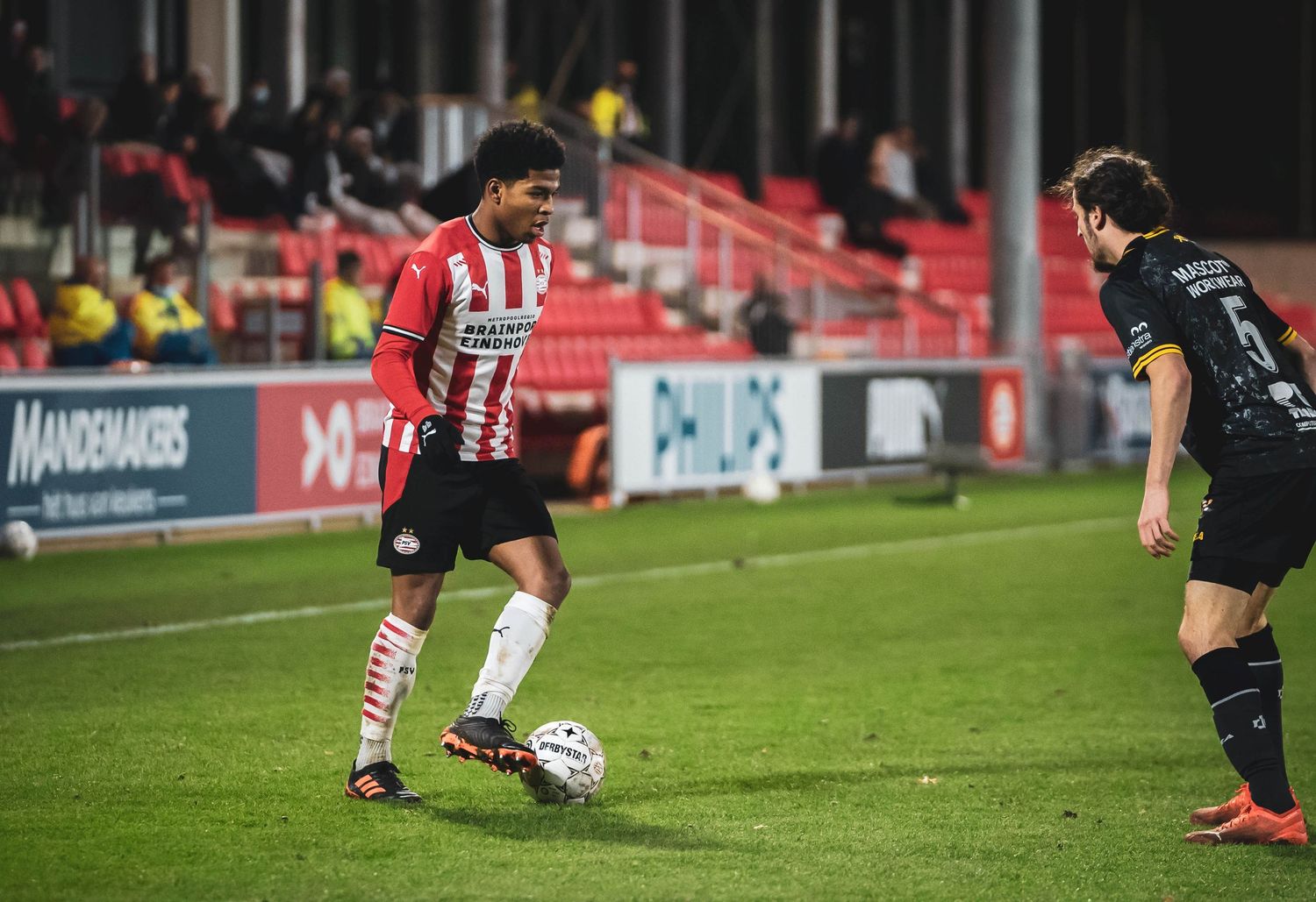 Soccer players compete under stadium lights with advertising boards visible in the background.