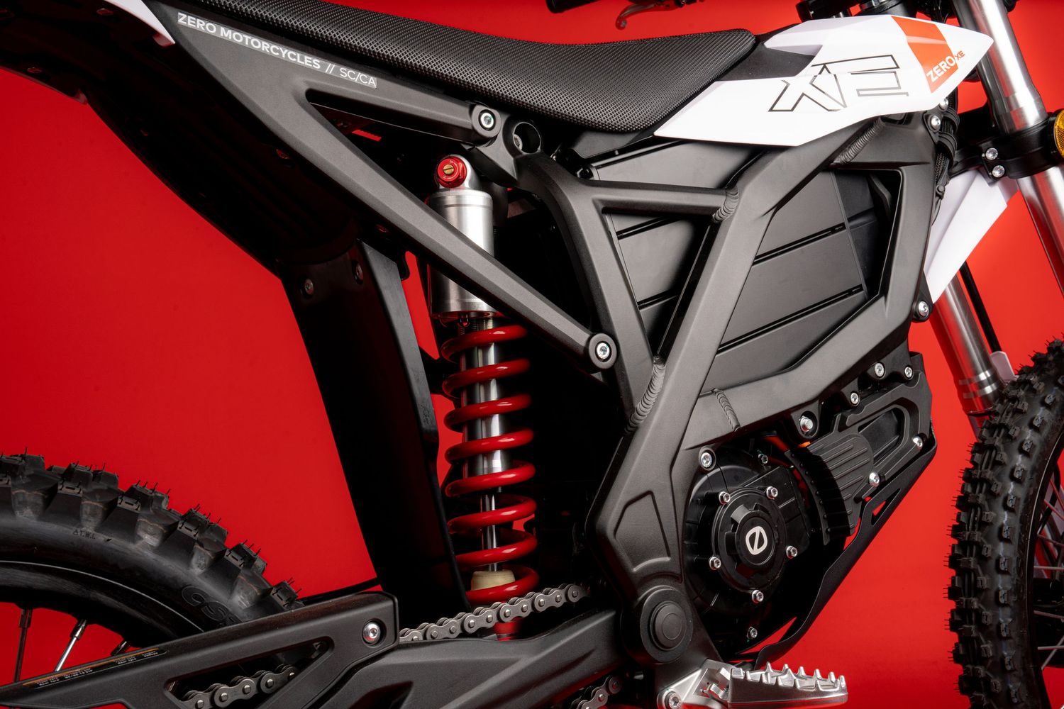 Close-up detail of electric motorcycle suspension and frame components against red background.