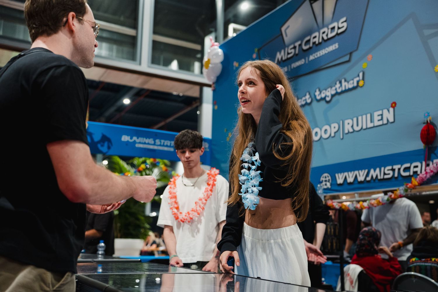 Two people shaking hands at a Mist Cards gaming booth during a card trading event.