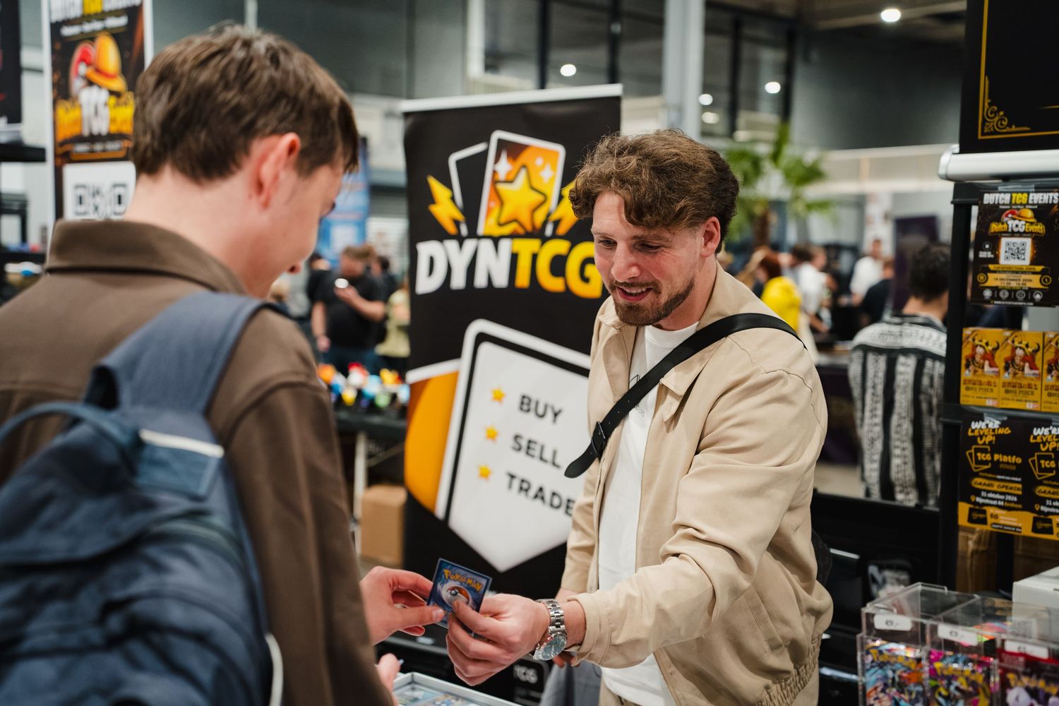 Two people trading cards at a DYN TCG buy sell trade booth at a gaming convention.
