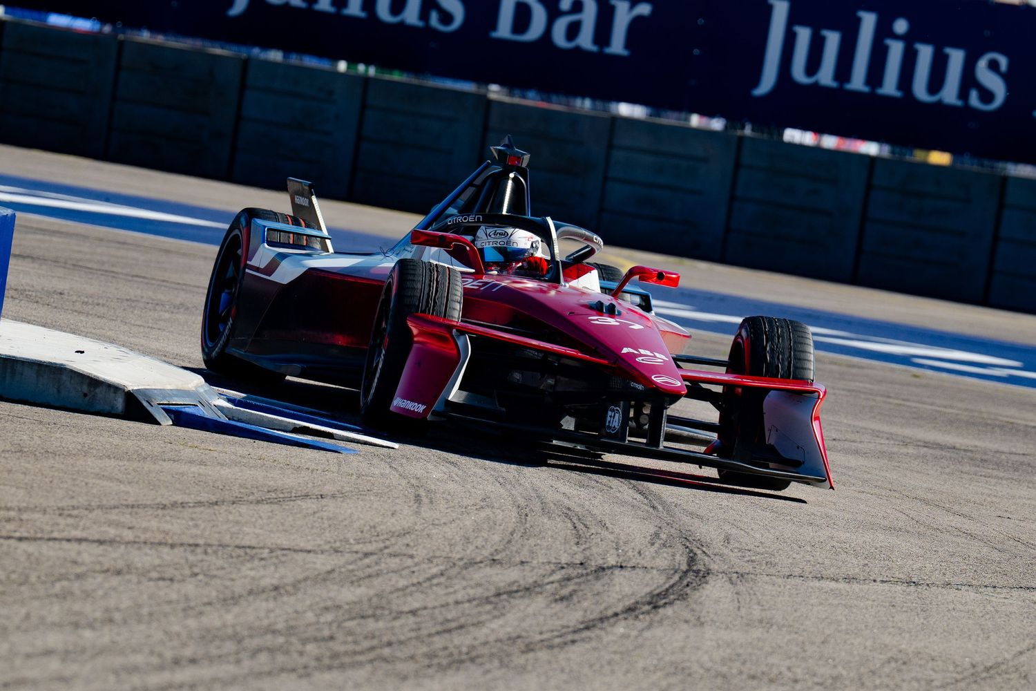 A red Formula E electric racing car navigates a street circuit corner during a competitive race event.