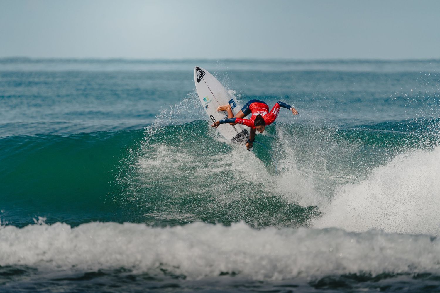 Surfer performing aerial maneuver on turquoise wave with dramatic splash.