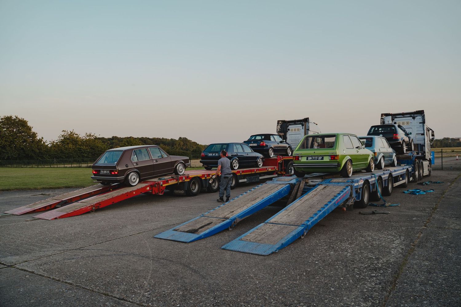 Car transport trucks with loading ramps at sunset preparing to load vehicles.
