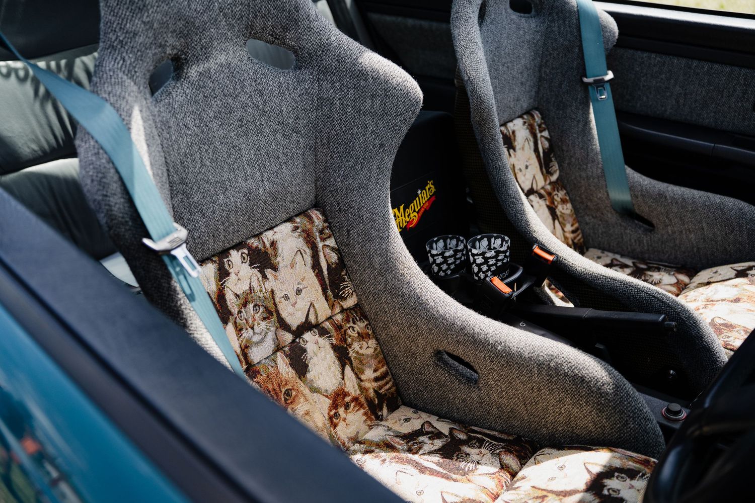 Custom car interior with gray bucket racing seats and floral patterned floor mats in a teal vehicle.
