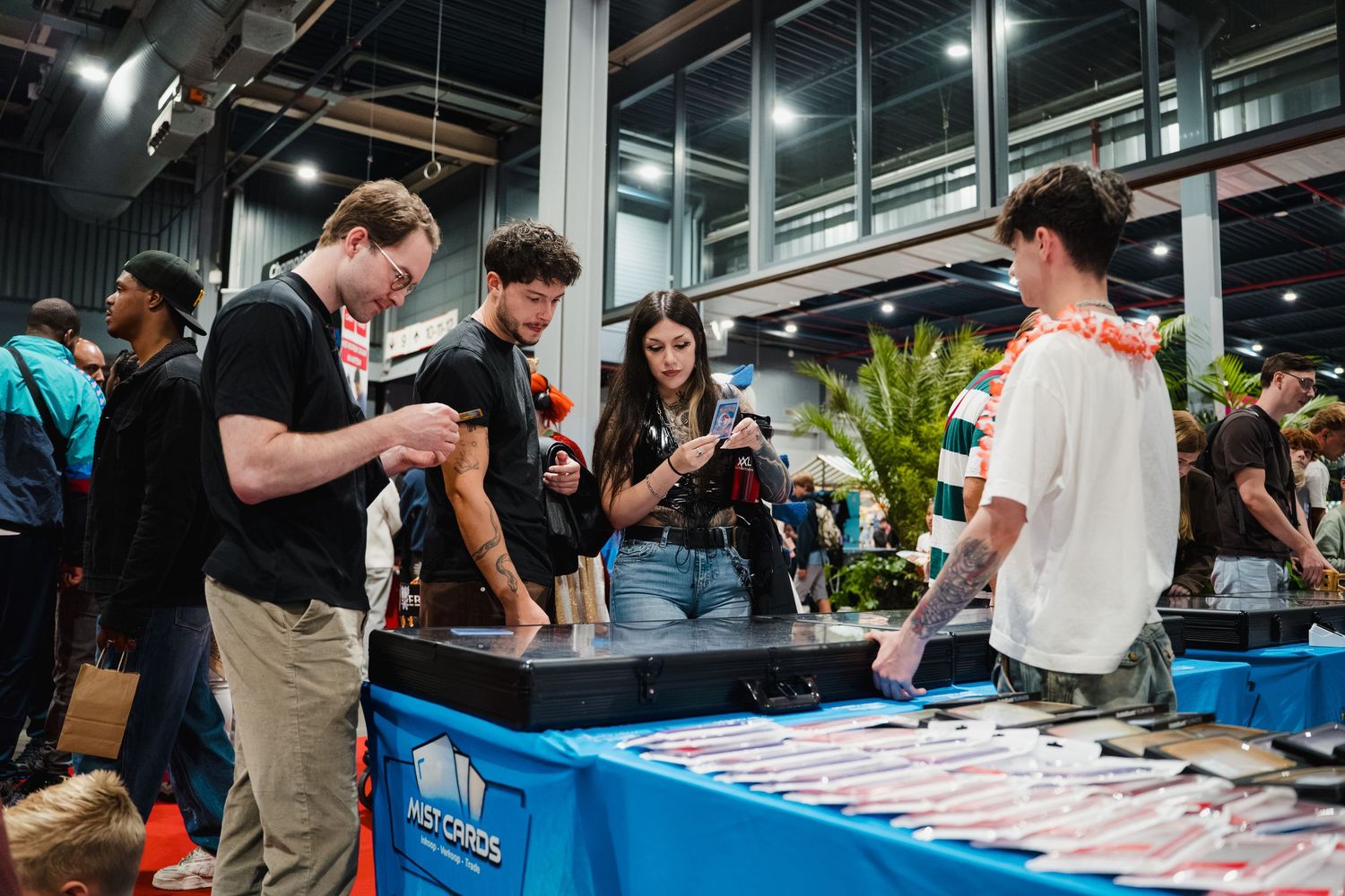 People browsing trading cards at a convention booth display table indoors.