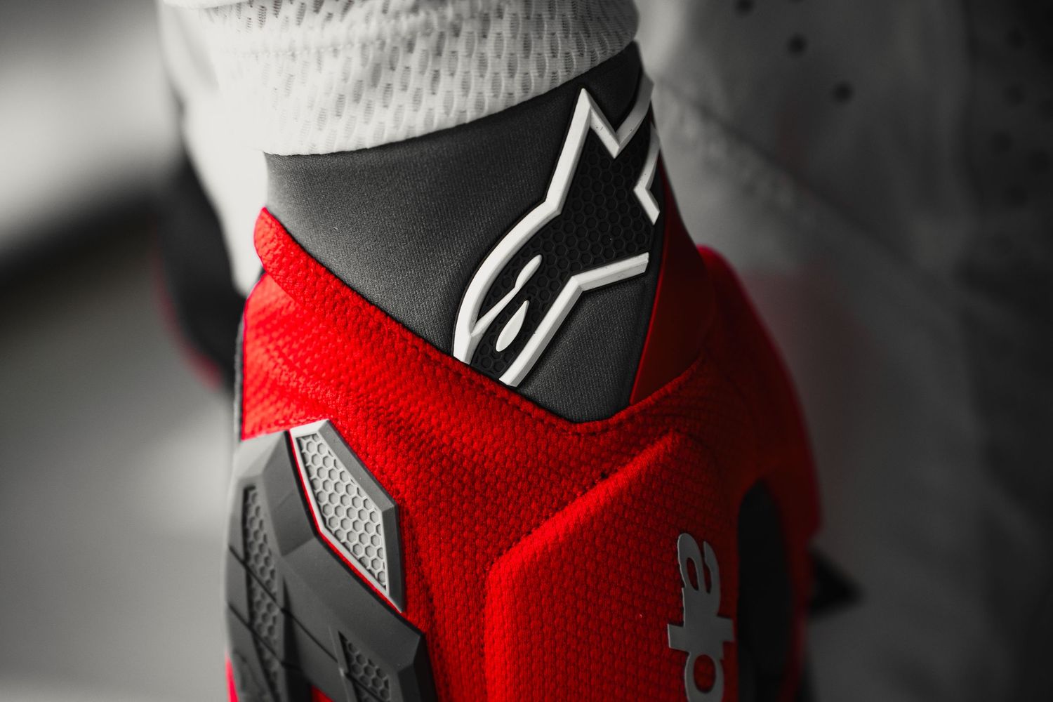 Close-up of red and black Alpinestars motorcycle boot featuring the iconic logo on protective ankle guard.