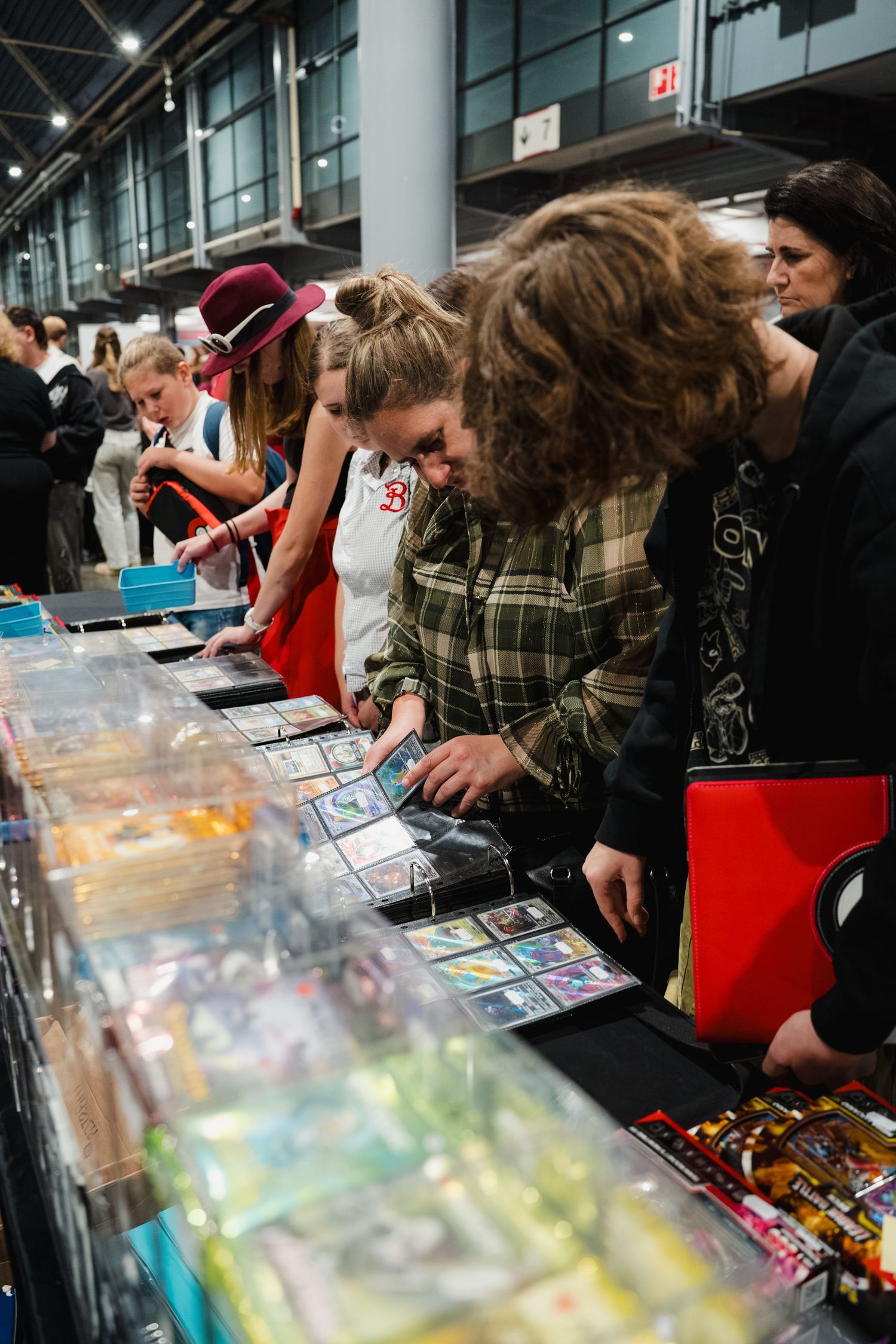 People browsing trading cards at a convention vendor table in a large indoor exhibition hall.