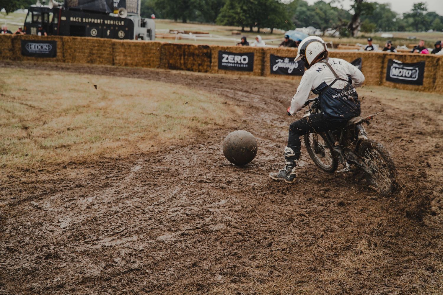 Motorcycle rider maneuvering around a large ball on a dirt racing course.
