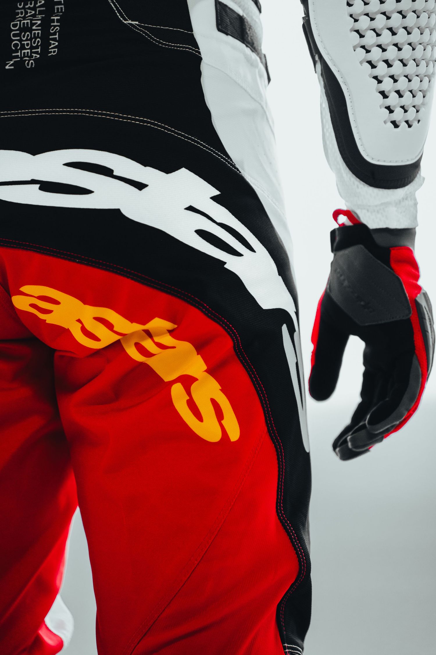 Alpinestars motocross racing gear featuring red pants with gold logo, black jacket, and red gloves on a rider.