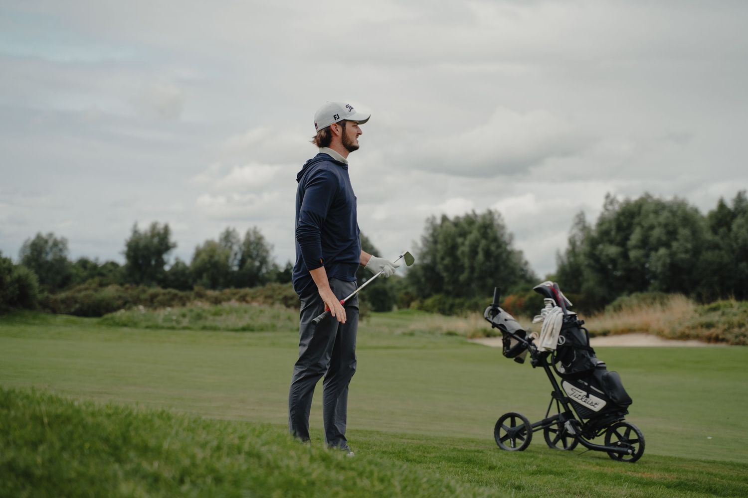 Scenic golf course landscape with players walking across green fairways and rolling hills.