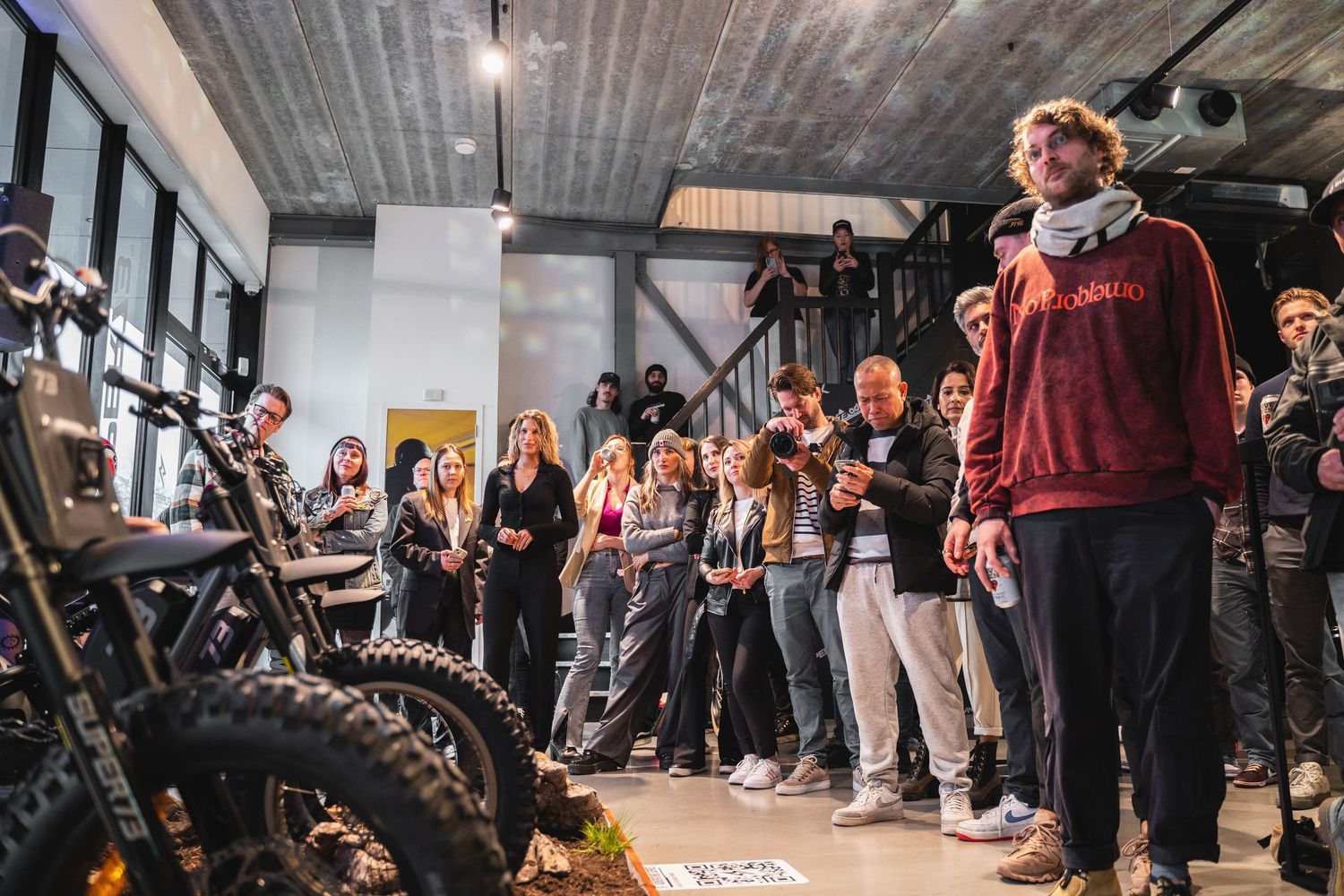 Crowd gathered in an industrial-style space for a motorcycle event or presentation.